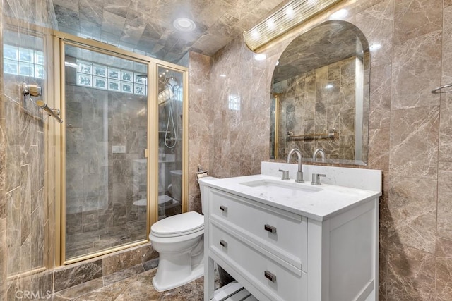 bathroom with tile walls, a shower stall, vanity, and toilet