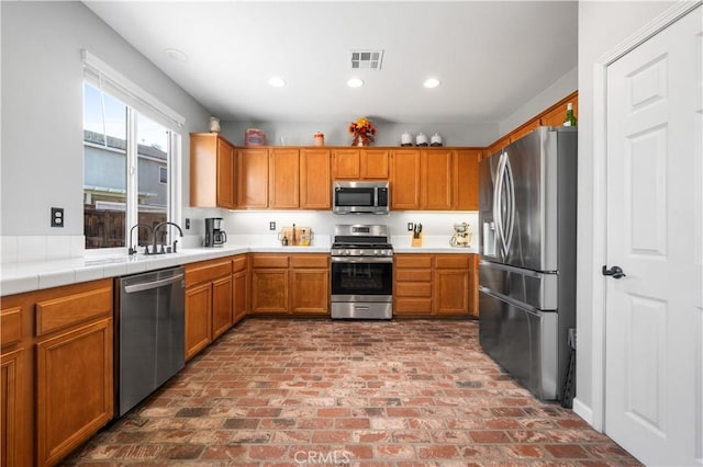 kitchen featuring visible vents, appliances with stainless steel finishes, a sink, light countertops, and brick floor