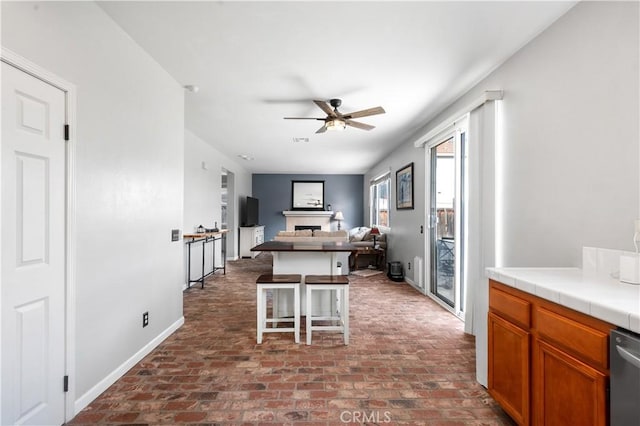 kitchen featuring a kitchen breakfast bar, a ceiling fan, brick floor, a fireplace, and tile counters
