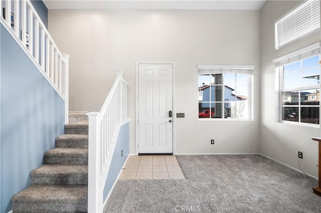 foyer featuring tile patterned flooring, baseboards, a high ceiling, stairway, and carpet