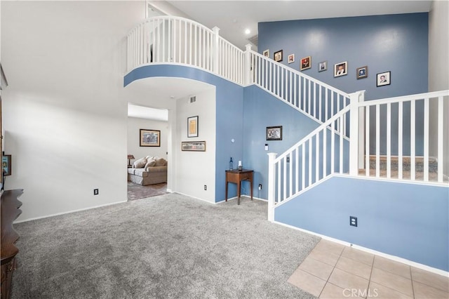 unfurnished living room with a high ceiling, carpet floors, stairs, baseboards, and visible vents