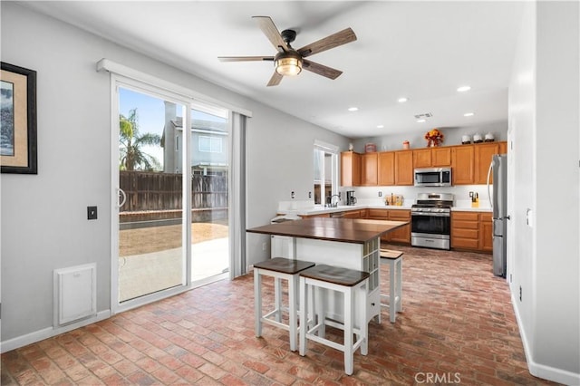 kitchen with a ceiling fan, baseboards, brick floor, stainless steel appliances, and recessed lighting