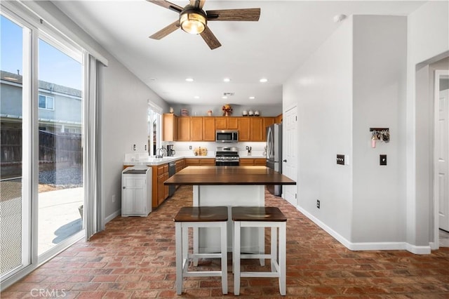kitchen featuring baseboards, brick floor, ceiling fan, and stainless steel appliances