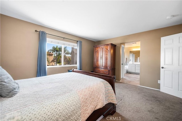 bedroom with baseboards, light carpet, and ensuite bath