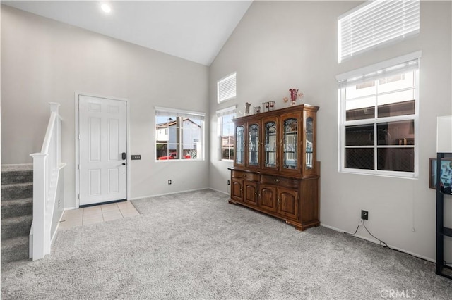 foyer entrance with stairway, high vaulted ceiling, baseboards, and carpet flooring