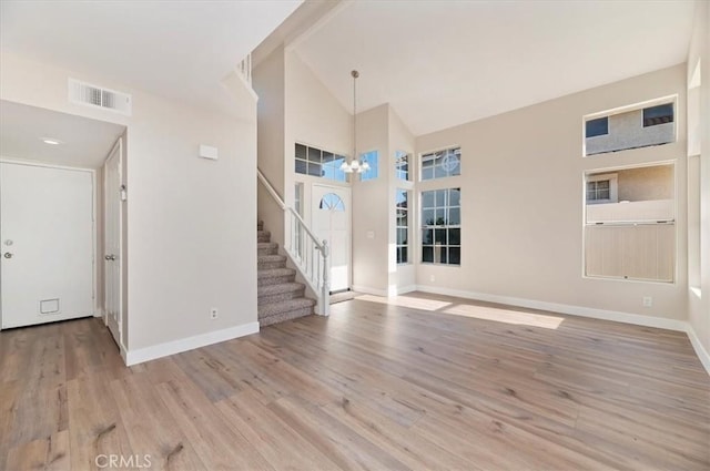 unfurnished living room with visible vents, an inviting chandelier, stairs, wood finished floors, and baseboards