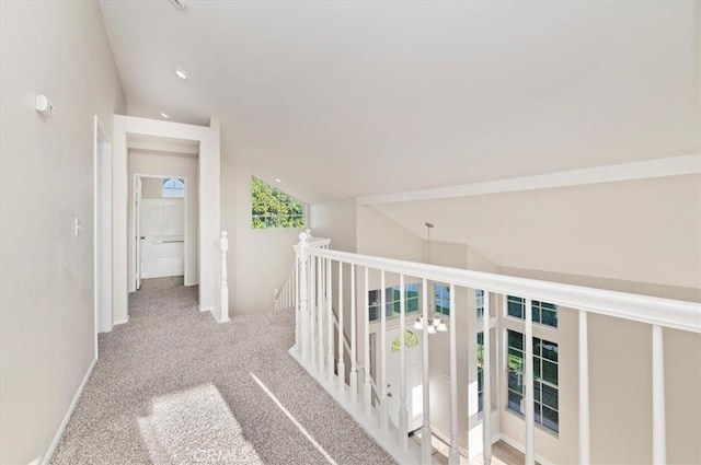 hall featuring carpet flooring, vaulted ceiling, and an upstairs landing