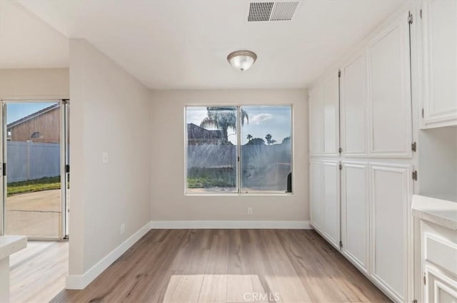 unfurnished dining area with baseboards, light wood-type flooring, and visible vents