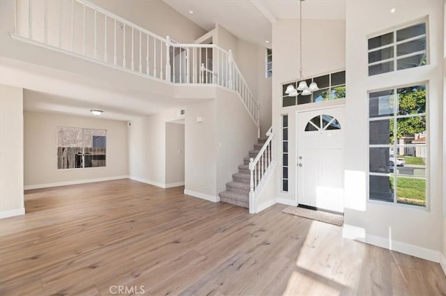 foyer with a towering ceiling, wood finished floors, stairway, baseboards, and a chandelier