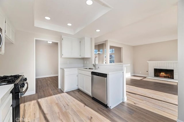 kitchen featuring dishwasher, a sink, light countertops, black gas range oven, and light wood-style flooring