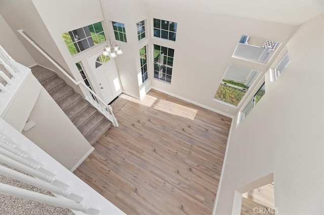 entrance foyer featuring a towering ceiling, wood finished floors, stairway, baseboards, and an inviting chandelier