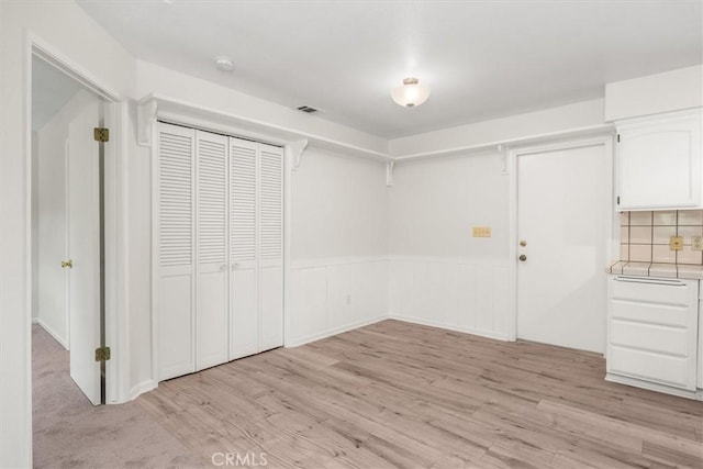 interior space featuring visible vents, light wood finished floors, wainscoting, and a closet