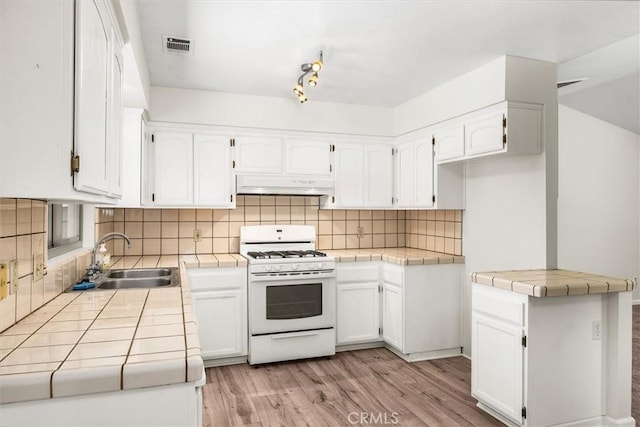 kitchen featuring a sink, tile counters, white cabinetry, white gas stove, and under cabinet range hood