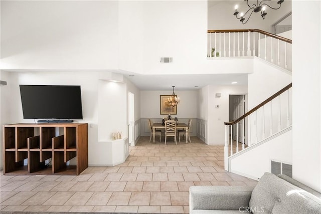 tiled living area with an inviting chandelier, a high ceiling, stairway, and visible vents