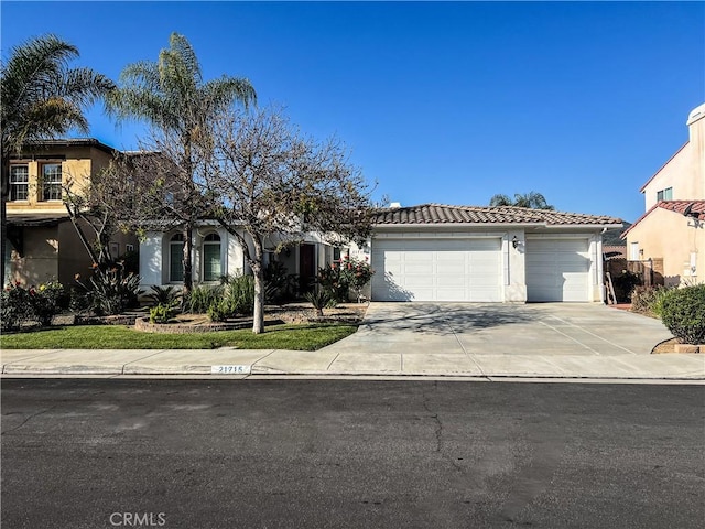 mediterranean / spanish-style home with an attached garage, stucco siding, a tile roof, and concrete driveway