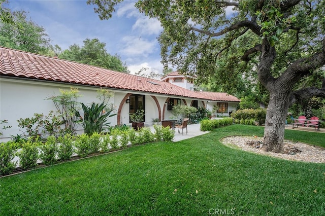 rear view of property featuring a yard, a tile roof, a patio area, and stucco siding