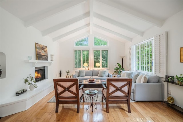 living room with a lit fireplace, vaulted ceiling with beams, and light wood-type flooring