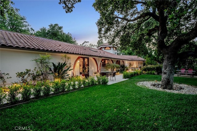 rear view of house with a tiled roof, a yard, a patio area, and stucco siding