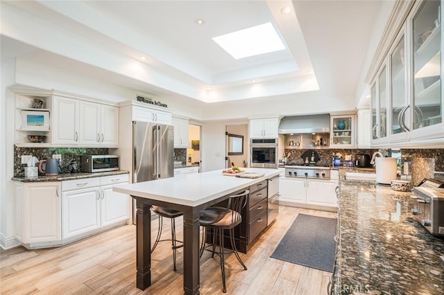 kitchen with stainless steel appliances, open shelves, a tray ceiling, and a center island