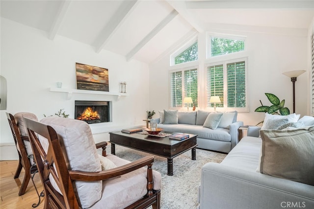 living room with high vaulted ceiling, beam ceiling, a lit fireplace, and light wood-style flooring