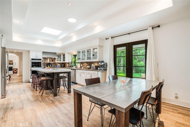 dining room with light wood finished floors, arched walkways, french doors, baseboards, and a tray ceiling
