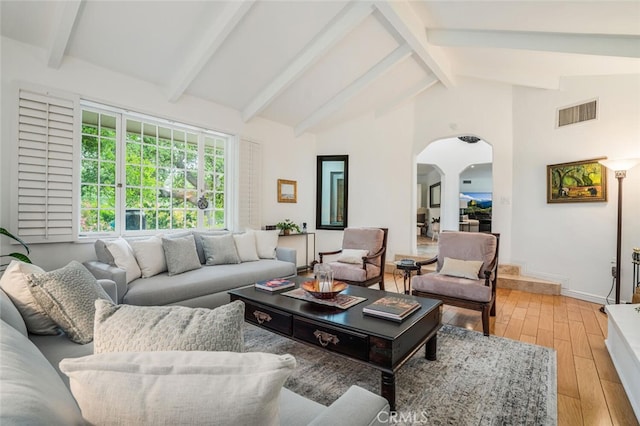 living room with beam ceiling, light wood-style floors, arched walkways, baseboards, and visible vents
