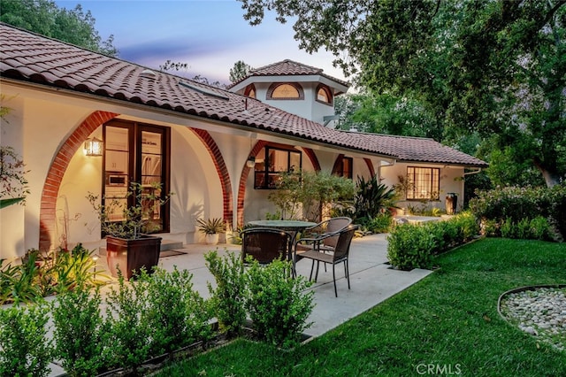 back of property featuring a yard, a tiled roof, a patio area, and stucco siding