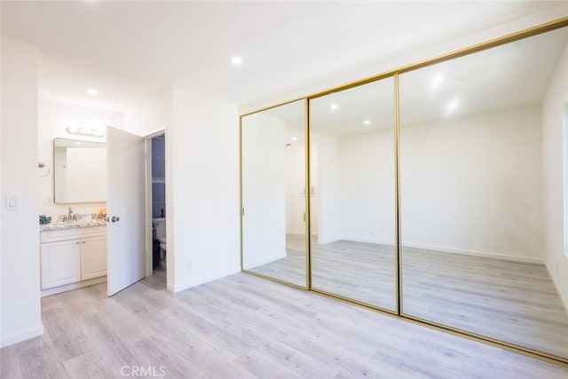 unfurnished bedroom featuring a closet, recessed lighting, a sink, light wood finished floors, and ensuite bath