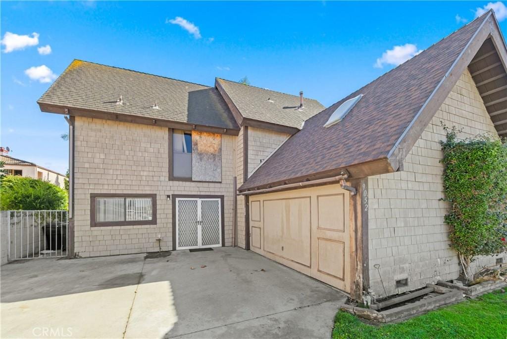 rear view of house featuring a patio, a shingled roof, and fence