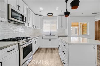 kitchen featuring a sink, light countertops, light wood-style flooring, stainless steel microwave, and white range with gas cooktop