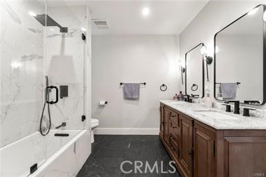 bathroom featuring shower / bath combination with glass door, double vanity, toilet, baseboards, and visible vents