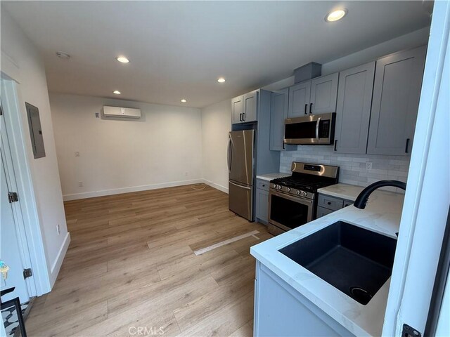 kitchen featuring light stone counters, appliances with stainless steel finishes, a sink, a wall mounted air conditioner, and baseboards