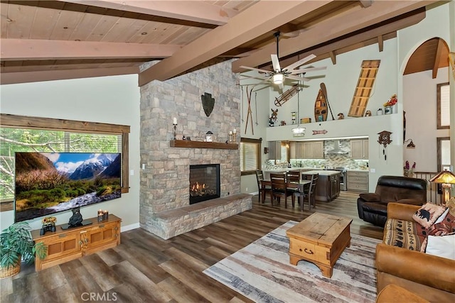 living area featuring ceiling fan, beam ceiling, a fireplace, baseboards, and wood finished floors