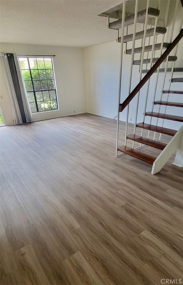 unfurnished living room with stairs, a textured ceiling, and wood finished floors