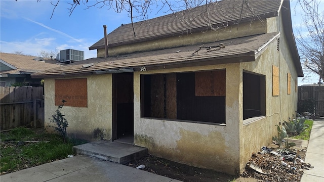 rear view of property featuring central air condition unit, fence, and stucco siding