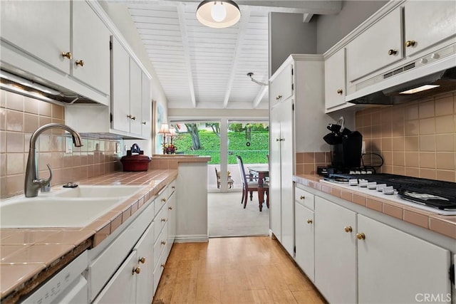 kitchen featuring tile counters, white cabinetry, under cabinet range hood, a sink, and light wood-style flooring