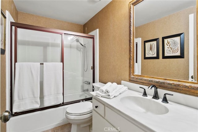 bathroom with toilet, a textured wall, shower / bath combination with glass door, and vanity
