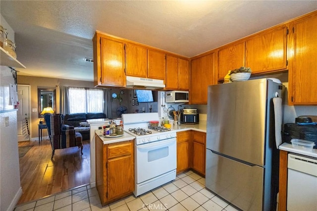 kitchen featuring light countertops, brown cabinetry, under cabinet range hood, and white appliances