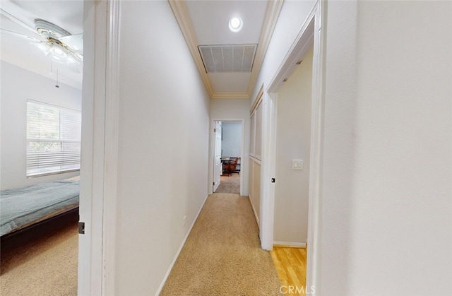 hall with light colored carpet, attic access, baseboards, visible vents, and ornamental molding