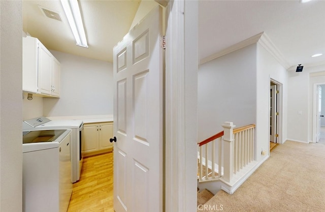 washroom with visible vents, crown molding, light colored carpet, washing machine and clothes dryer, and cabinet space