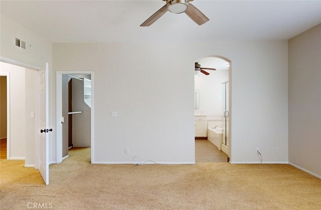 unfurnished bedroom featuring visible vents, arched walkways, baseboards, connected bathroom, and light carpet