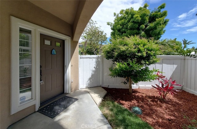view of exterior entry featuring fence and stucco siding