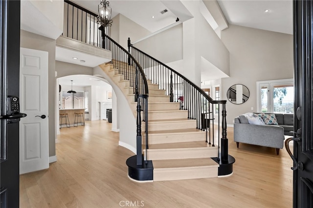 stairway featuring visible vents, wood finished floors, baseboards, high vaulted ceiling, and arched walkways