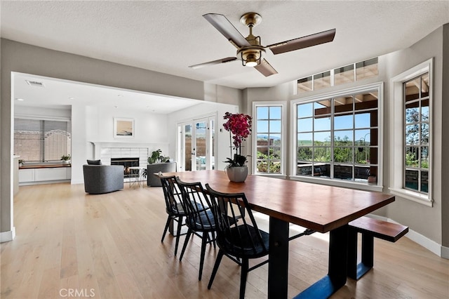 dining space featuring a brick fireplace, baseboards, a textured ceiling, a ceiling fan, and light wood finished floors