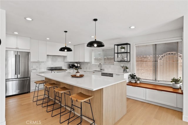 kitchen with a kitchen island, appliances with stainless steel finishes, tasteful backsplash, a sink, and light countertops