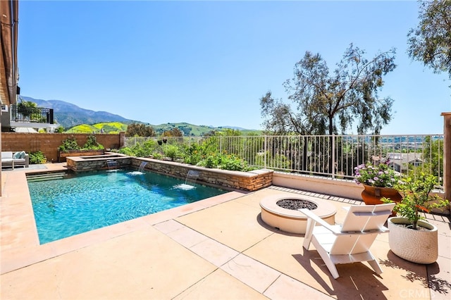 view of swimming pool with a pool with connected hot tub, a fenced backyard, a mountain view, a patio, and a fire pit