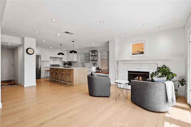 living area featuring a fireplace, recessed lighting, light wood-style flooring, and visible vents