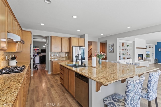 32701 Juniper Berry Dr, Winchester, CA 92596 - kitchen featuring stainless steel appliances, under cabinet range hood, wood finished floors, a kitchen island with sink, and light stone countertops