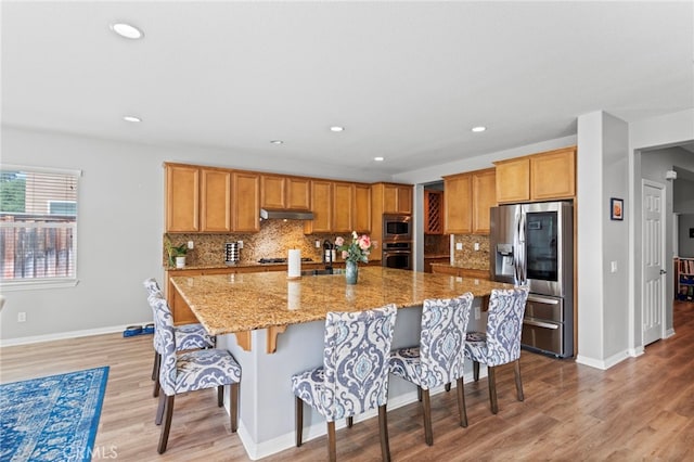 32701 Juniper Berry Dr, Winchester, CA 92596 - kitchen with appliances with stainless steel finishes, under cabinet range hood, a breakfast bar, tasteful backsplash, and light wood-type flooring