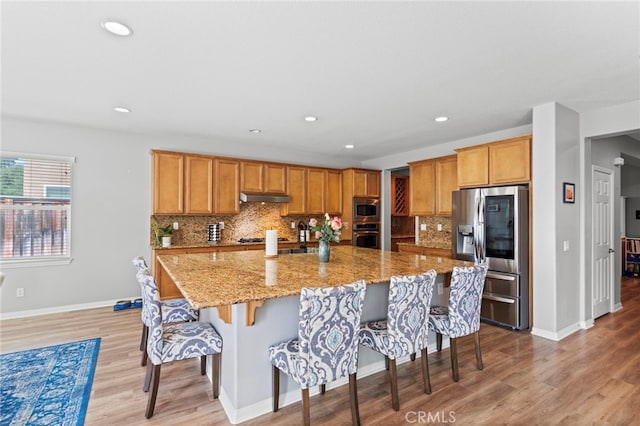 32701 Juniper Berry Dr, Winchester, CA 92596 - kitchen with stainless steel appliances, under cabinet range hood, a kitchen bar, decorative backsplash, and light wood-style flooring